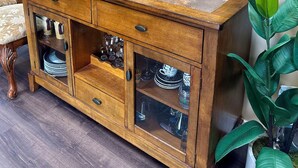 Un gabinete de madera con puertas de cristal, una planta en maceta y un cuadro en la pared.
