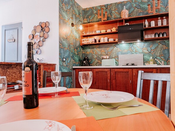 A dining area with a table set for two, a bottle of wine, and a decorative wall with a leaf pattern.