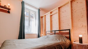 A bedroom with a bed, a window with curtains, wooden paneling on the walls, and a bedside table with a lamp. - Spacious cottage near Éguzon Lake (Orsennes)