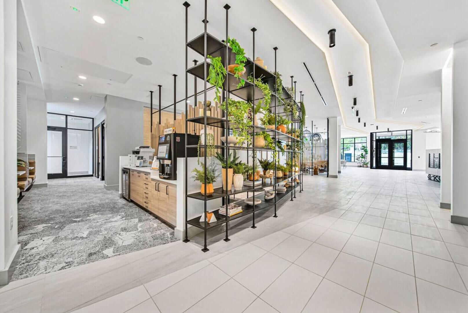 Een moderne lobby met een plantenpresentatie in het midden, een receptiebalie en een ruim gebied met betegelde vloer.