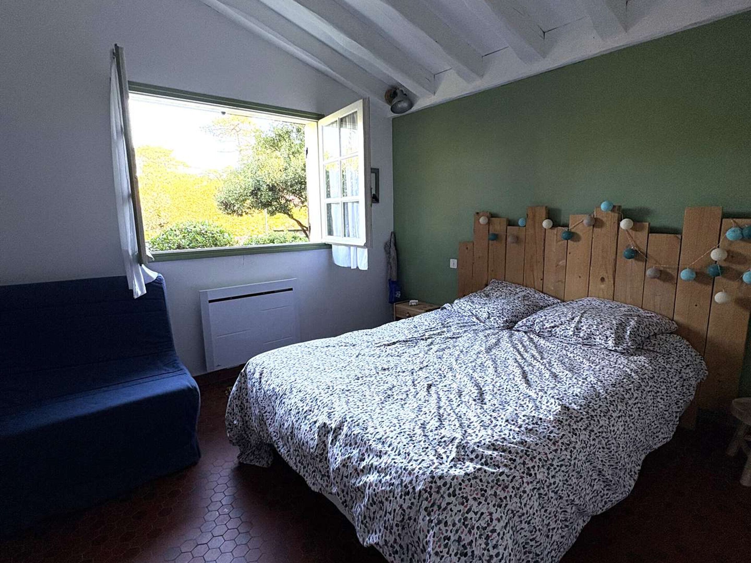 A bedroom with a bed, a window, a radiator, and a wooden headboard.