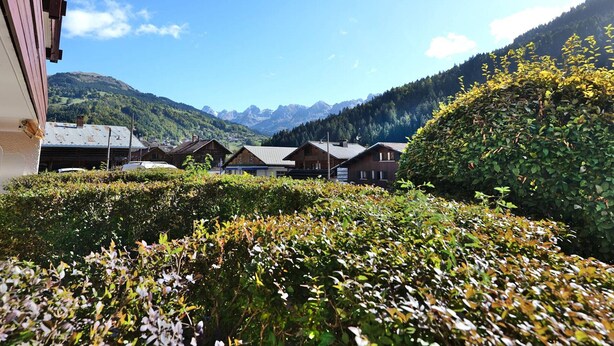 A mountain village with traditional wooden houses, a clear sky, and a view of distant mountains.