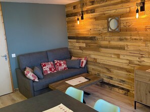 Una sala de estar moderna con un sofá gris, paneles de madera, una mesita de madera y un sillón azul claro.