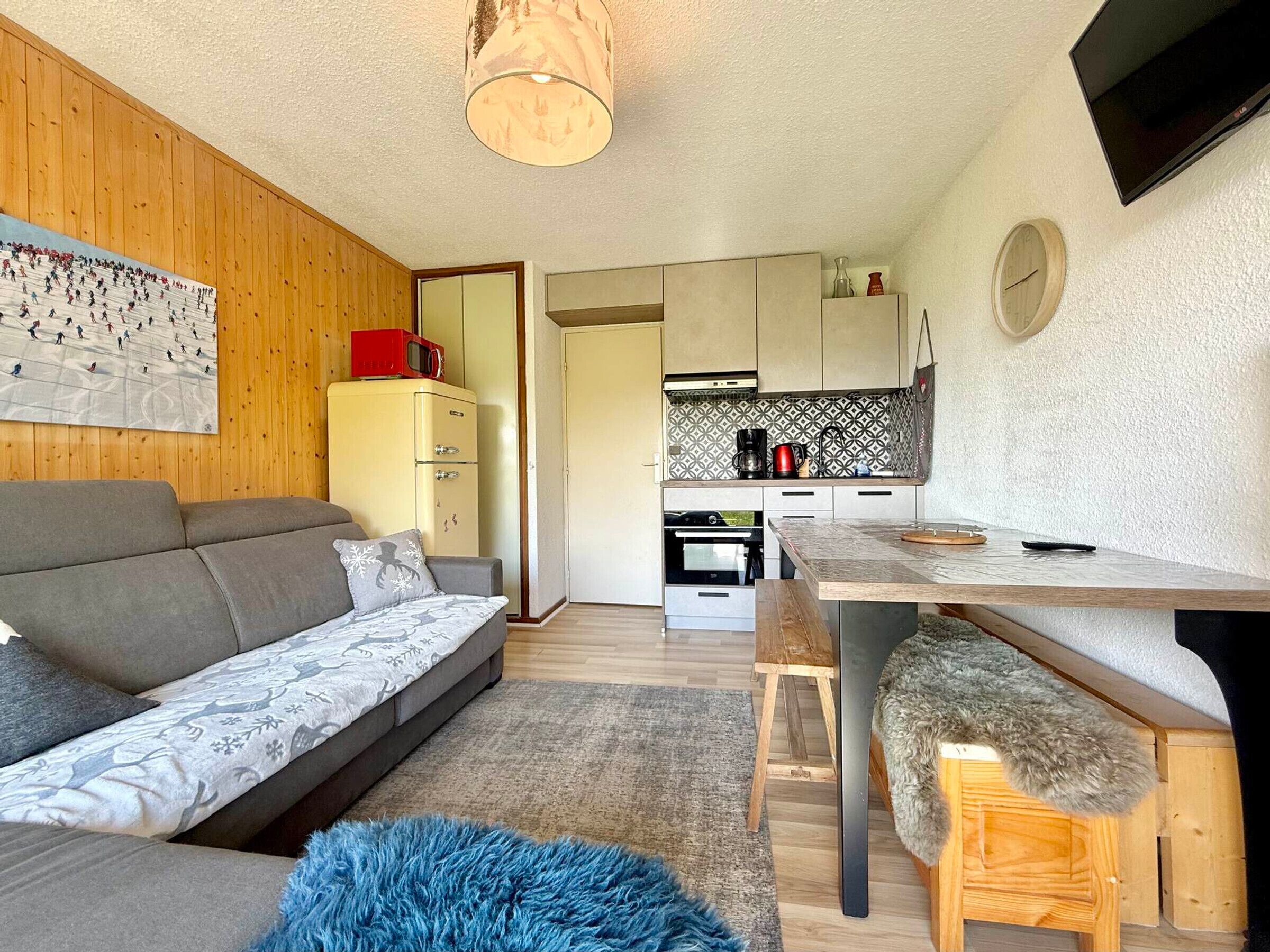 Ein kompakter Wohnraum mit einer Couch, einem Esstisch, einer Küchenzeile und einer Holzbalkendecke.
