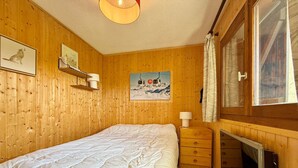 A wooden room with a bed, a dresser, a mounted picture, and a window with curtains.
