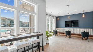 A modern hotel lobby with large windows, a pool view, a bar area, and a seating area with a TV. - Landing | Stunning 1BD, Gym, Yoga Studio (Myrtle Beach)