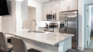 A modern kitchen with white cabinetry, stainless steel appliances, a granite countertop, and a built-in TV. - Landing | Stunning 1BD, Gym, Yoga Studio (Myrtle Beach)