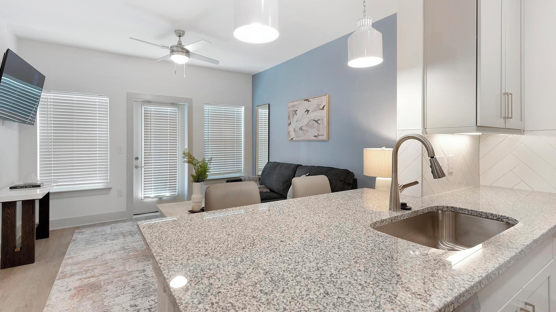 A modern kitchen with granite countertops, a stainless steel sink, and a ceiling fan.