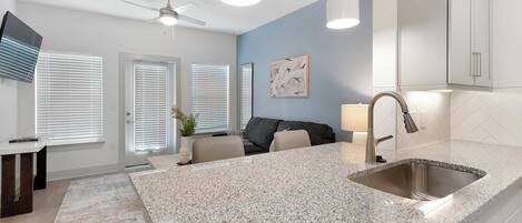 A modern kitchen with granite countertops, a stainless steel sink, and a ceiling fan.