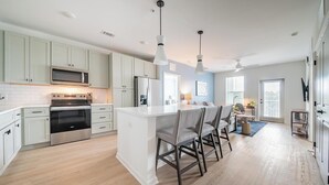 A modern kitchen with white cabinets, stainless steel appliances, and a central island with bar stools. - Landing | Beautiful 2BD, Pool (Palm Coast)