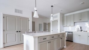 A modern kitchen with a central island, white cabinetry, and pendant lighting. - Landing | Beautiful 2BD, Pool (Palm Coast)