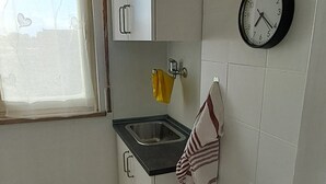 A small kitchen with white cabinets, a black countertop, a sink, a clock, and a window with a curtain. - Minimal suite - Novarese night (Novara)