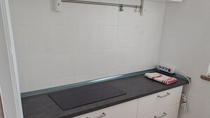 A kitchen with white cabinets, a black countertop, and a marble floor. There are shelves above the countertop holding a jar, a box, and a dish rack. - Minimal suite - Novarese night (Novara)