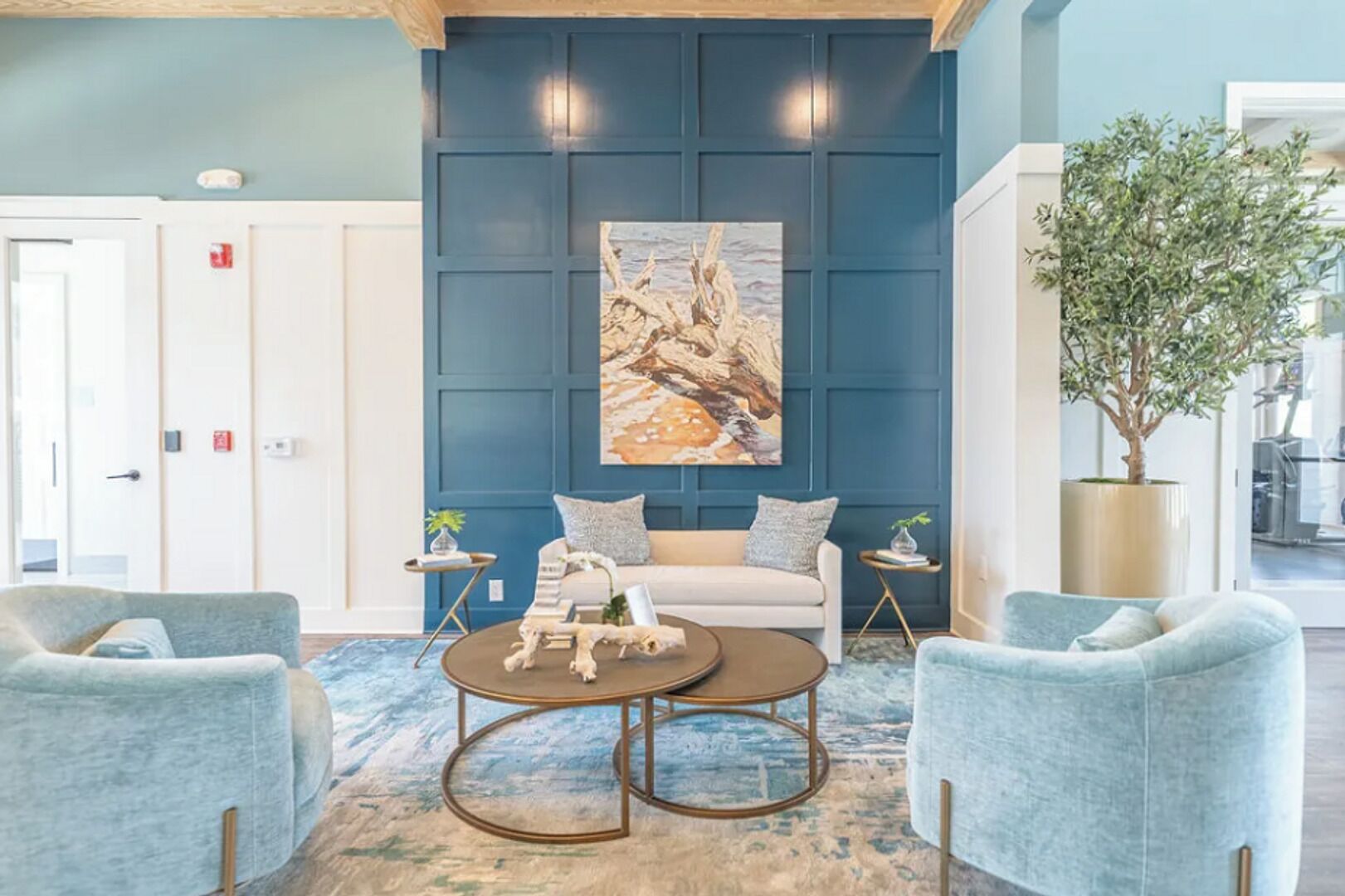 A modern lobby with a blue wall, a white sofa, two armchairs, a coffee table, and a large painting.