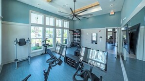 Una palestra con attrezzature da allenamento, ampie finestre e una ventola a soffitto.