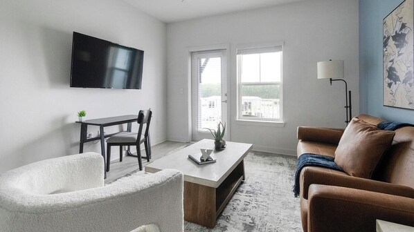 Un salon moderne comprenant un téléviseur à écran plat, une table à manger avec des chaises, un canapé, une table basse et un lampadaire.