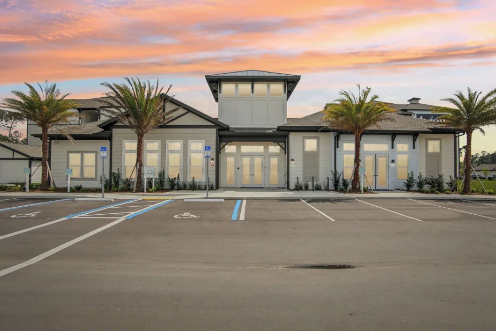 A parking lot with marked spaces for disabled access, a building with a central entrance, and palm trees.