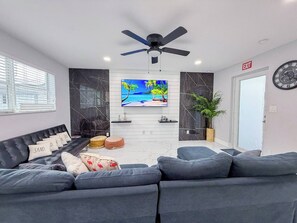 Un salon moderne avec un canapé gris, un ventilateur de plafond, un téléviseur et une plante.