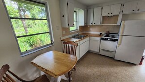 A kitchen with white cabinets, a wooden table, and a window with a view of greenery. - Paradise in the heart of Old Englewood Village (Englewood)