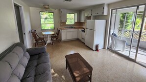 A compact living space with a sofa, dining table, chairs, a kitchen area with a refrigerator, stove, and sink, and a sliding glass door leading to an outdoor area. - Paradise in the heart of Old Englewood Village (Englewood)