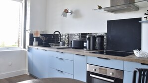 Moderni keittiö, jossa on vaaleansiniset kaapit, musta työtaso ja ruostumattomasta teräksestä valmistetut kodinkoneet.