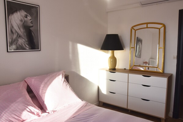 Un dormitorio con cama, cómoda, lámpara y un cuadro en la pared.