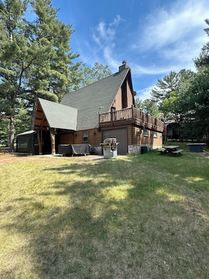 A log cabin with a sloped roof, a covered porch, and a picnic table in the yard.