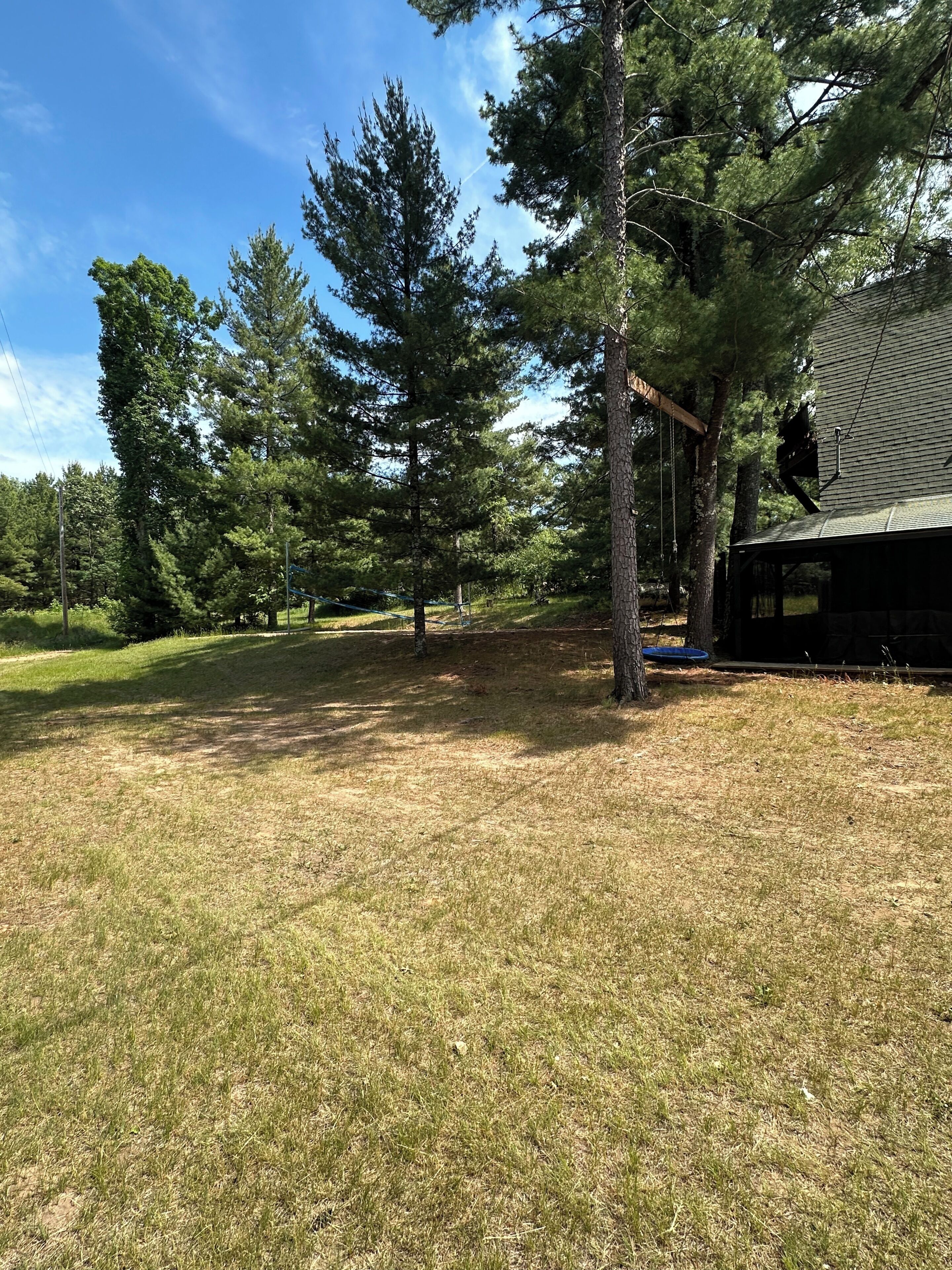 A grassy yard with trees, a swing set, and a building with a sloped roof.