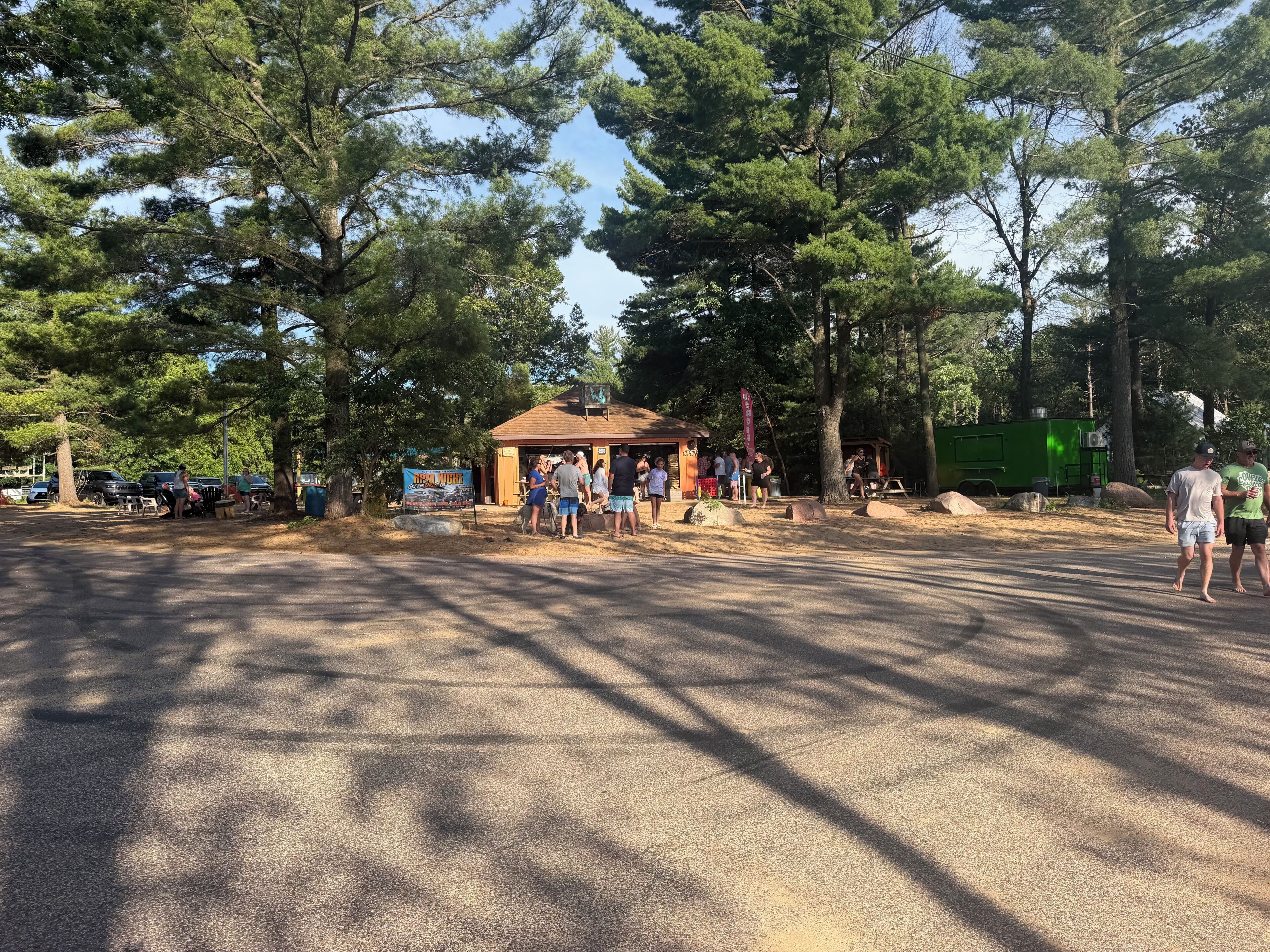 A parking area with a small building, surrounded by trees.