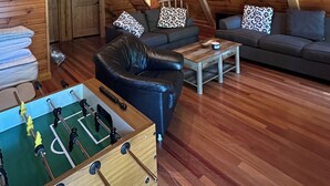 Een zolderkamer met een schuin houten plafond, een kroonluchter, een zithoek, een bijzettafeltje en een tafelvoetbaltafel.