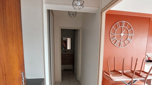 A hallway with a wooden door, a tiled floor, a ceiling light fixture, and a wall clock. - Studio ideally located (Sens)