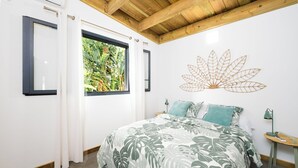 Een slaapkamer met een bed, een raam met gordijnen, een wanddecoratie en een nachtkastje.