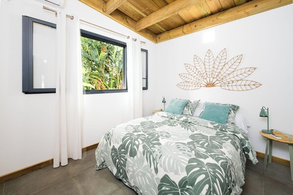 Une chambre à coucher avec un lit, une fenêtre avec des rideaux, un élément de décoration murale et une table de chevet.
