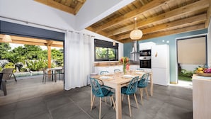 Een moderne keuken met een eethoek, houten balken in het plafond en uitzicht op een zwembad en tuin.