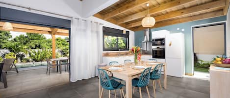 Une cuisine moderne avec un coin repas, des poutres apparentes en bois au plafond et une vue sur une piscine et un jardin.