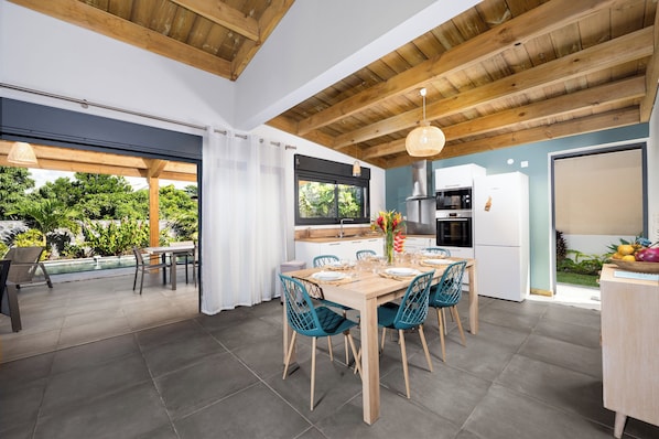 Una cocina moderna con comedor, vigas de madera en el techo y vistas a una piscina y jardín.