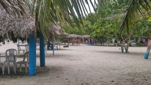 A beach area with thatched-roof structures, plastic chairs, and a sandy ground. - LA CASITA DE CHEPE - Iconic apartment in Gaspar Hernandez (Gaspar Hernández)
