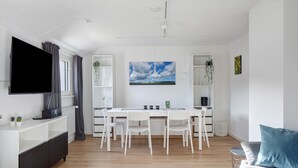 Ein modernes Wohnzimmer mit Flachbildfernseher, einem Esstisch mit Stühlen, einer Couch mit Kissen und einem Bild an der Wand.