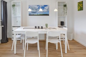 Et hvidt spisebord med fire stole, en hvid reol og et indrammet landskabsmaleri på væggen.