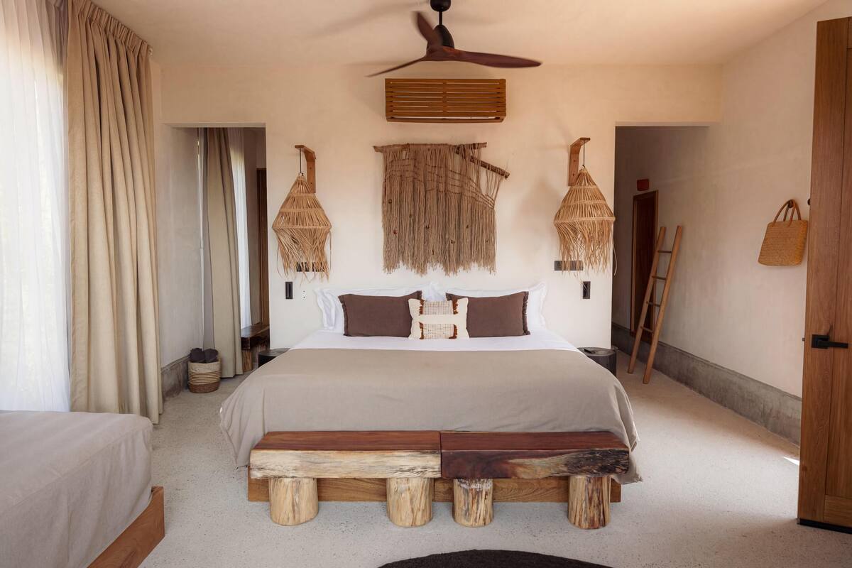 A bedroom with a large bed, wooden headboard, hanging woven baskets, and a ceiling fan.