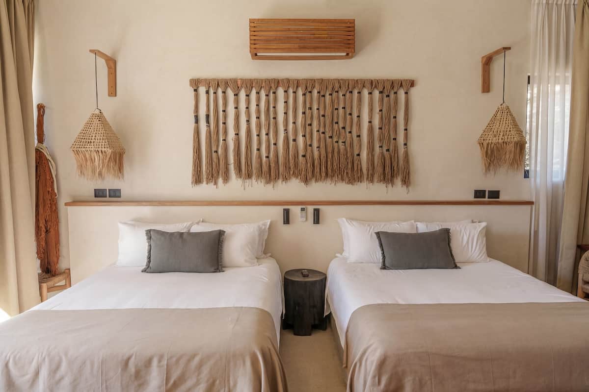 A hotel room with two beds, a wooden headboard, a wall-mounted tapestry, and a small round table.