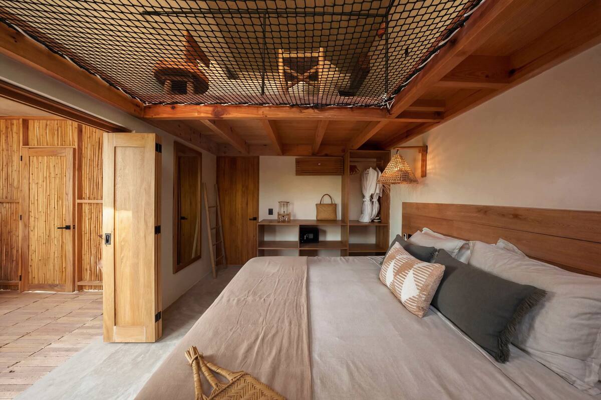 A room with a bed, wooden walls, a netted ceiling, and a wooden wardrobe.