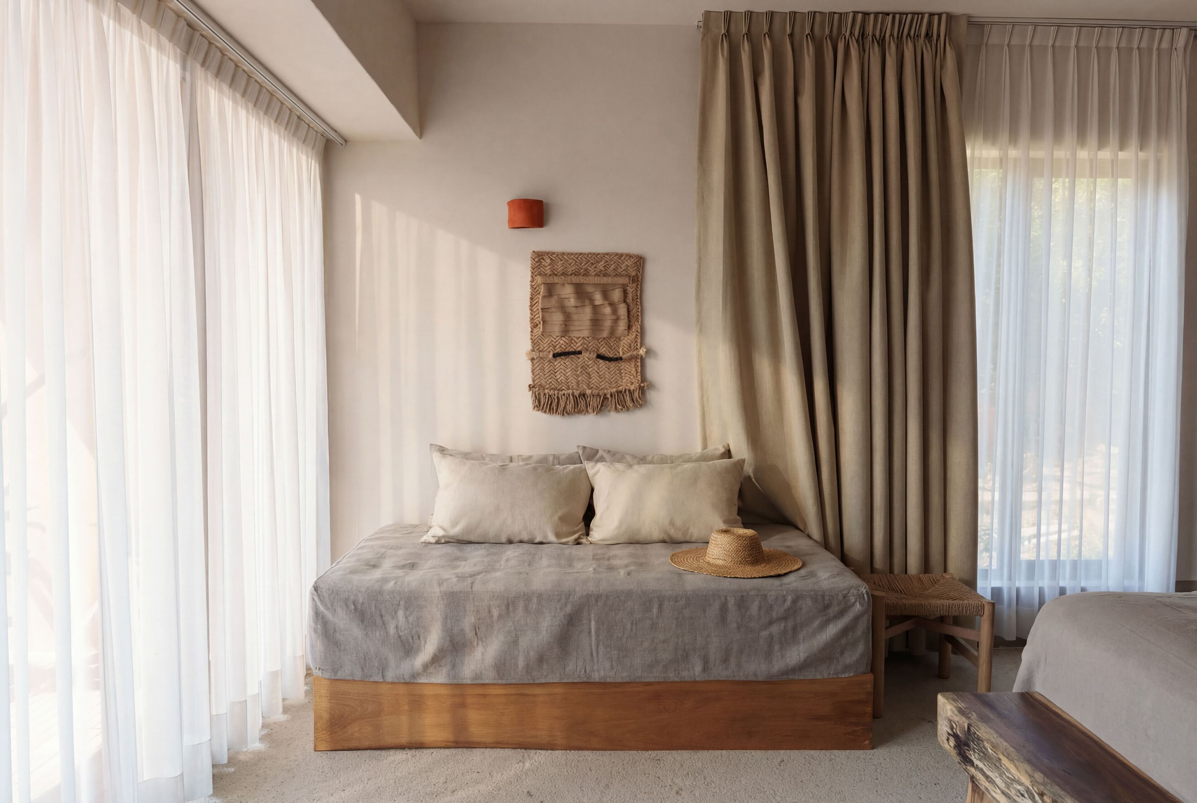 Een slaapkamer met een bed, een hoed, een wandkleed en een houten bankje.