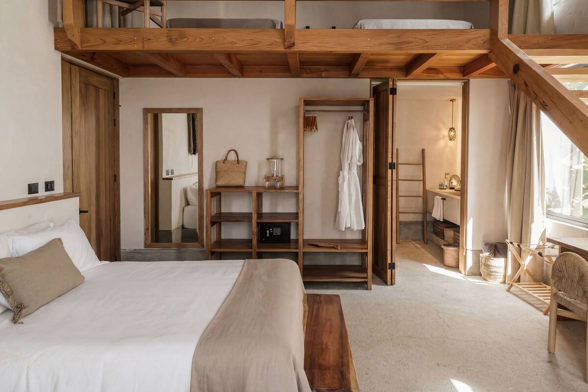 A bedroom with a large bed, wooden shelves, a wardrobe, and a small bathroom area.