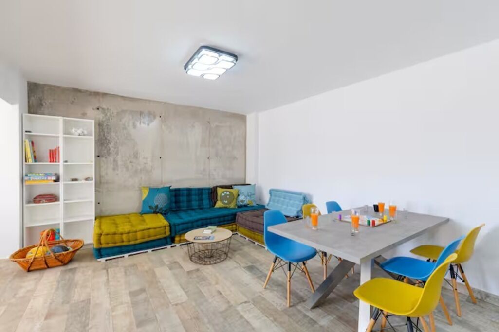 Een moderne woonkamer met een hoekbank, een eettafel met stoelen, een boekenkast en een wand van beton.