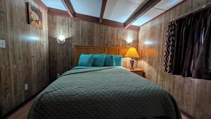 Ein Zimmer mit Holzwandverkleidung, einem Bett mit türkisfarbenen Kissen, einem Holz-Kopfteil, einem Nachttisch mit Lampe und einem Fenster mit Vorhängen.