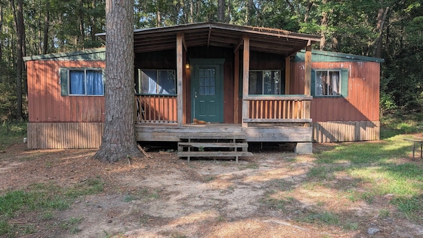 Eine rustikale Holzhütte mit grüner Tür, einer Holzveranda und einem kleinen Vorgarten.
