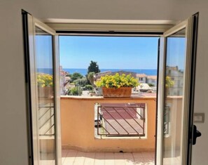 A balcony with a view of the sea and buildings, a potted plant, and a metal railing. - Kalon Eidos. The magical place of Ionian Calabria (San Carlo-Condofuri Marina)