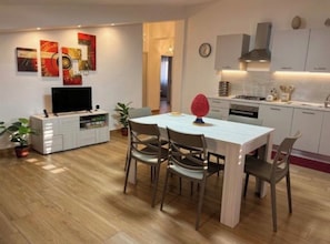 A modern kitchen with white cabinets, a dining area with a white table and chairs, and a flat-screen TV on a white cabinet. - Kalon Eidos. The magical place of Ionian Calabria (San Carlo-Condofuri Marina)
