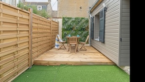 A wooden deck with a table and chairs, surrounded by a wooden fence and a green wall.